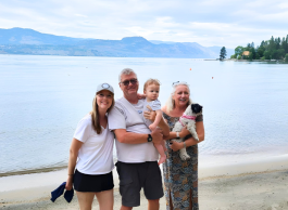 A happy family of four stands in front of the lake and beach