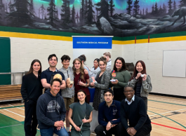A group of young people in casual clothing post in front of a banner that says Southern Medical Program in a school gymnasium.