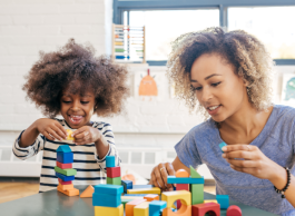 a little girl plays with wooden building blocks with her mother