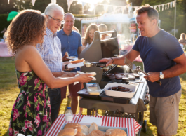 A group of people huddled around a table with BBQ and food and fill up their plates. 