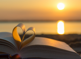 A book on a beach at sunset with two pages folded into the shape of a heart.