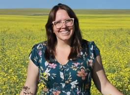 Person in a blue floral dress standing in a vast yellow flower field under a clear blue sky.