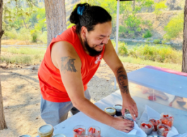 a person prepares food outside while smiling and wearing an orange shirt