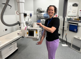 A health-care worker smiles in front of an X-ray machine.