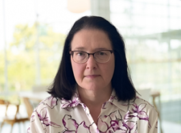a person wearing glasses and a white and purple shirt looks to camera