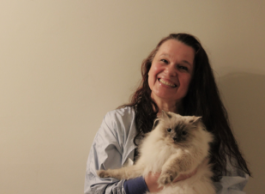 A smiling person with long, dark hair poses for a picture while holding a white cat.