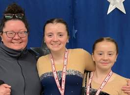 A mother standing with her two daughters wearing skating competition medals. 