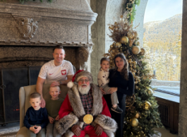 A family of five, two parents and three children, pose with Santa Claus next to a Christmas tree.