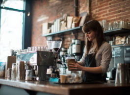 A person in an apron holds a paper cup behind the counter at a coffee shop.