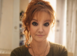 a person with red hair and a green shirt looks to camera while sitting inside a room 