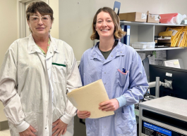 Two people in lab coats, one white, one blue, stand together in a lab.