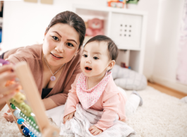 A parent and their baby play on the floor in a bedroom. They are looking at an abacus.