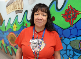 A person with a red t-shirt on stands in front of Indigenous art mural inside hospital.
