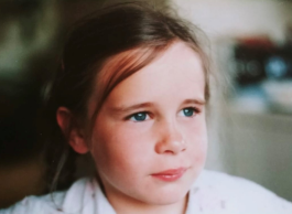 A young child with brown hair pulled back in a ponytail looks pensively away from the camera.