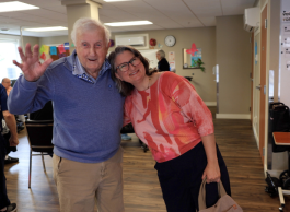 An old man and his daughter smiling and waving at camera.