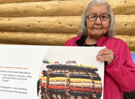 Person holding a display board featuring a photograph of a handcrafted birch bark basket during a community engagement event.